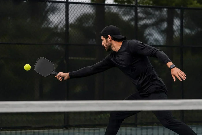 Joueur de pickleball effectuant un retour difficile en extension avec une raquette noire pour illustrer l'amélioration des réflexes.