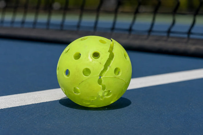 Balle de pickleball fissurée sur un terrain extérieur pendant un échange.