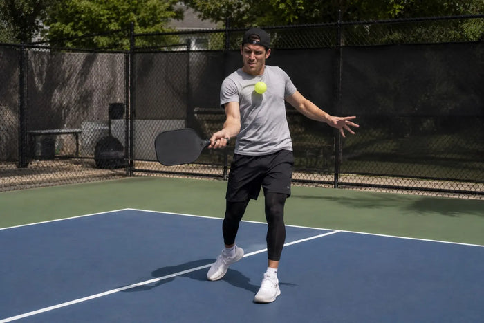 Joueur de pickleball en plein échange se faisant toucher par la balle sur un terrain de pickleball extérieur réaliste.