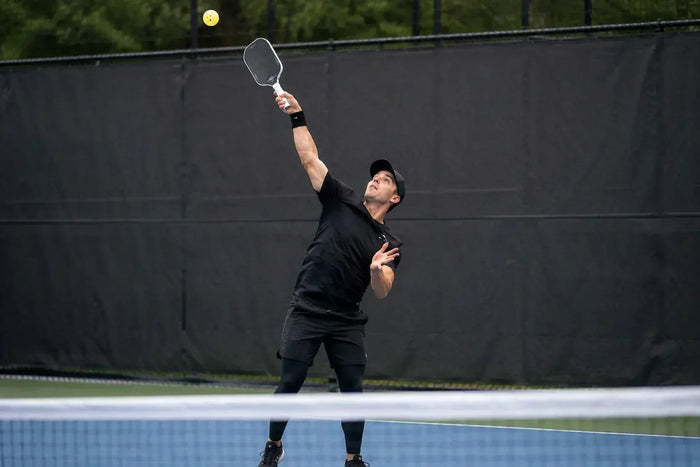 Joueur de pickleball réalisant un smash puissant au-dessus du filet lors d'un échange sur un terrain extérieur.