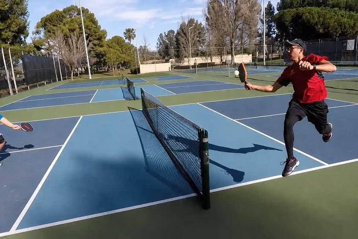 Joueur réalisant un coup Erne au pickleball près du filet sur un terrain extérieur.