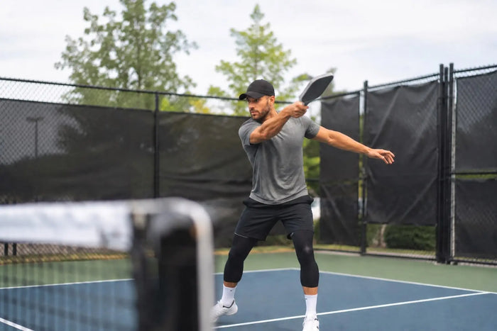 Joueur de pickleball préparant une frappe puissante sur un terrain extérieur