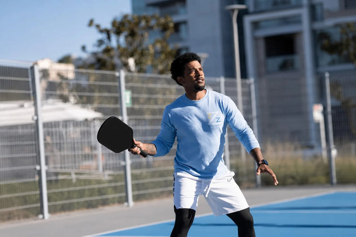 Joueur de pickleball tenant une raquette noire sur un terrain extérieur bleu lors d’un échange en plein soleil.