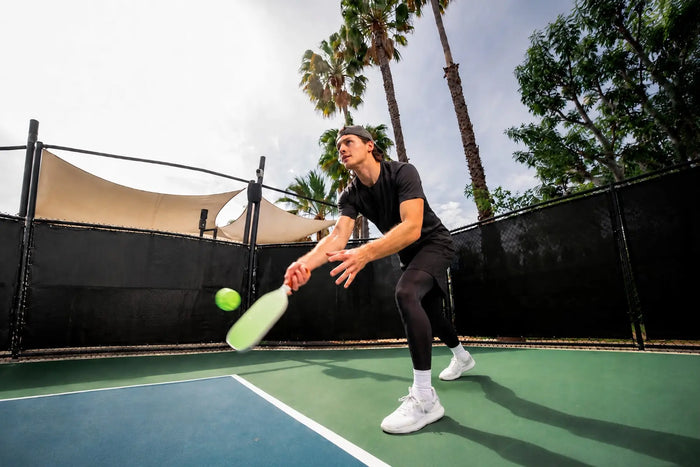 Joueur de pickleball portant un short et un legging de compression, prêt à recevoir une balle sur un terrain extérieur
