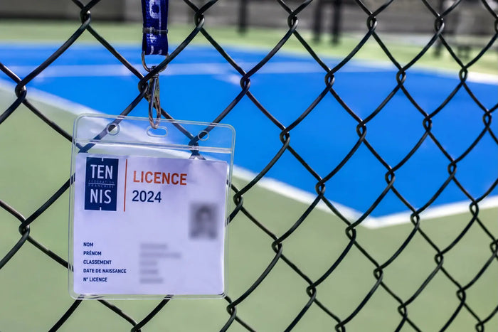 Badge de licence sportive suspendu devant un terrain de pickleball, illustrant la question de la licence FFT pour jouer au pickleball en France.