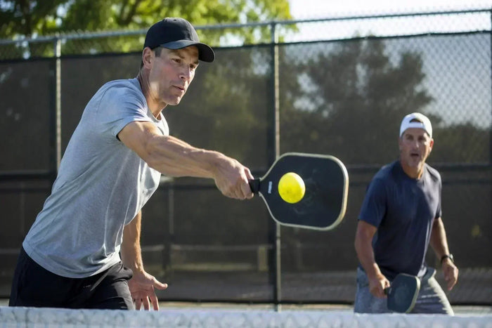 Joueur de pickleball frappant une balle lors d’un échange dynamique sur un terrain extérieur avec impact visible sur la raquette