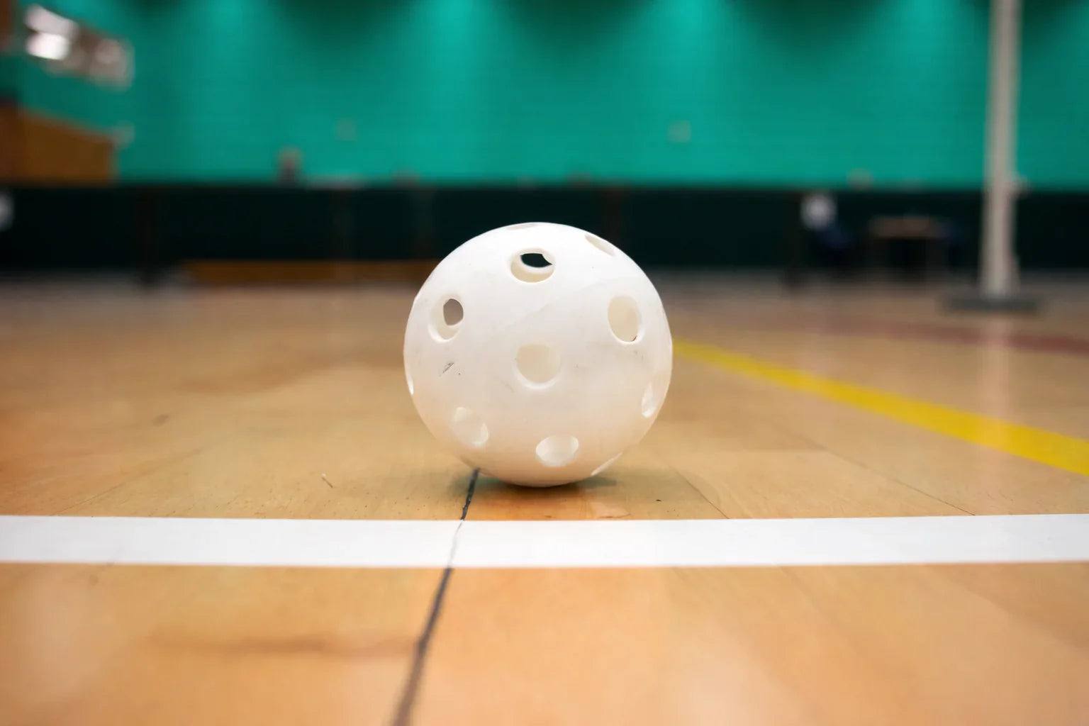 Balle de pickleball blanche pour l'intérieur posée sur un sol de gymnase en bois.