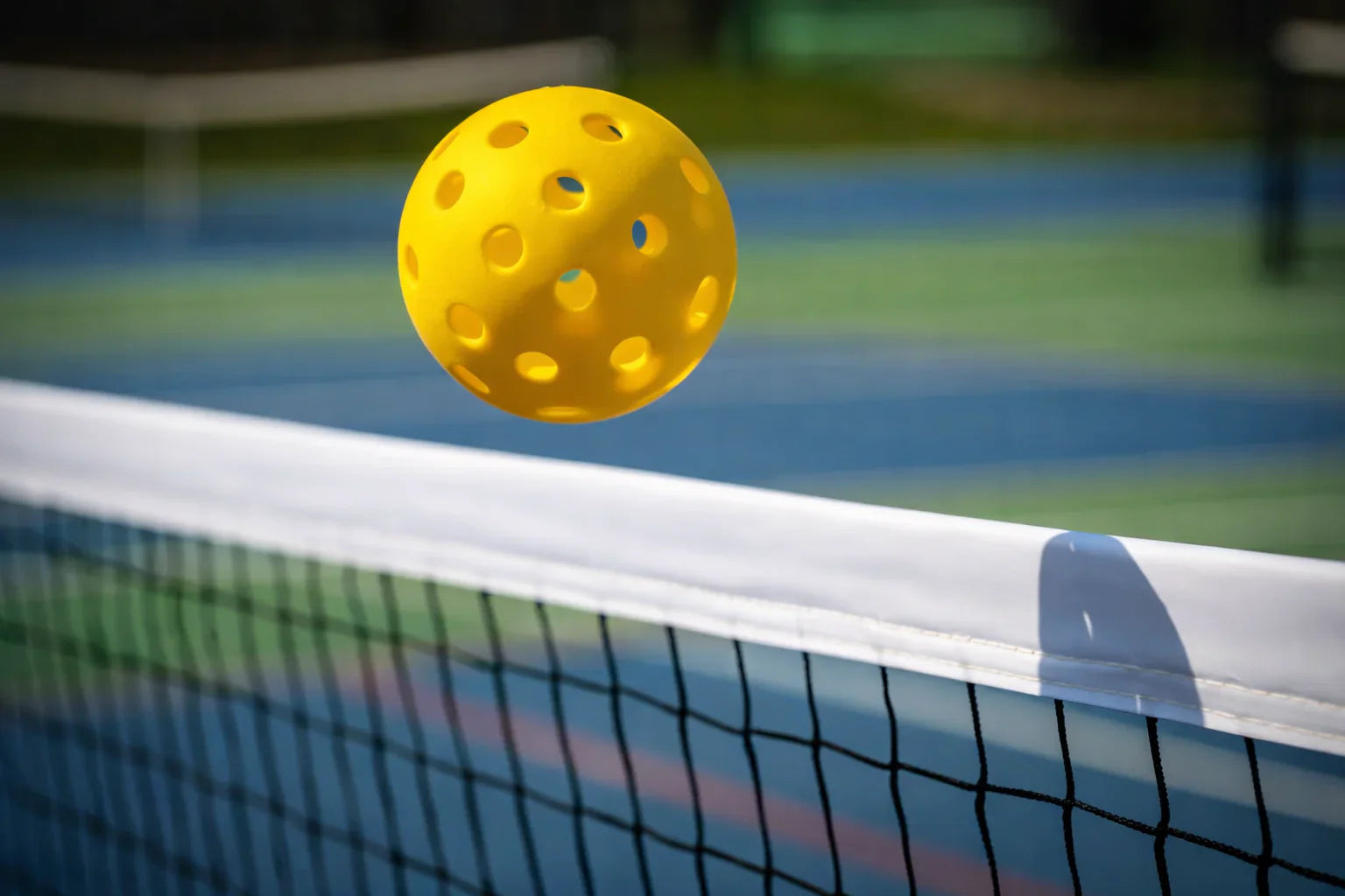 Balle de pickleball en plein vol au-dessus d'un filet de sport en extérieur.