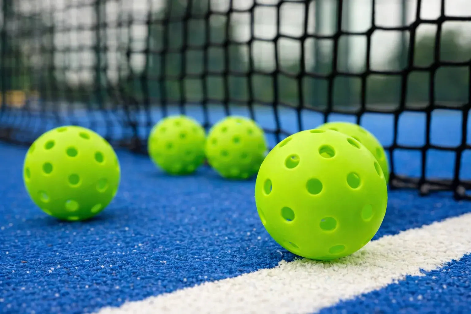 Assortiment de balles de pickleball sur un terrain bleu devant un filet.