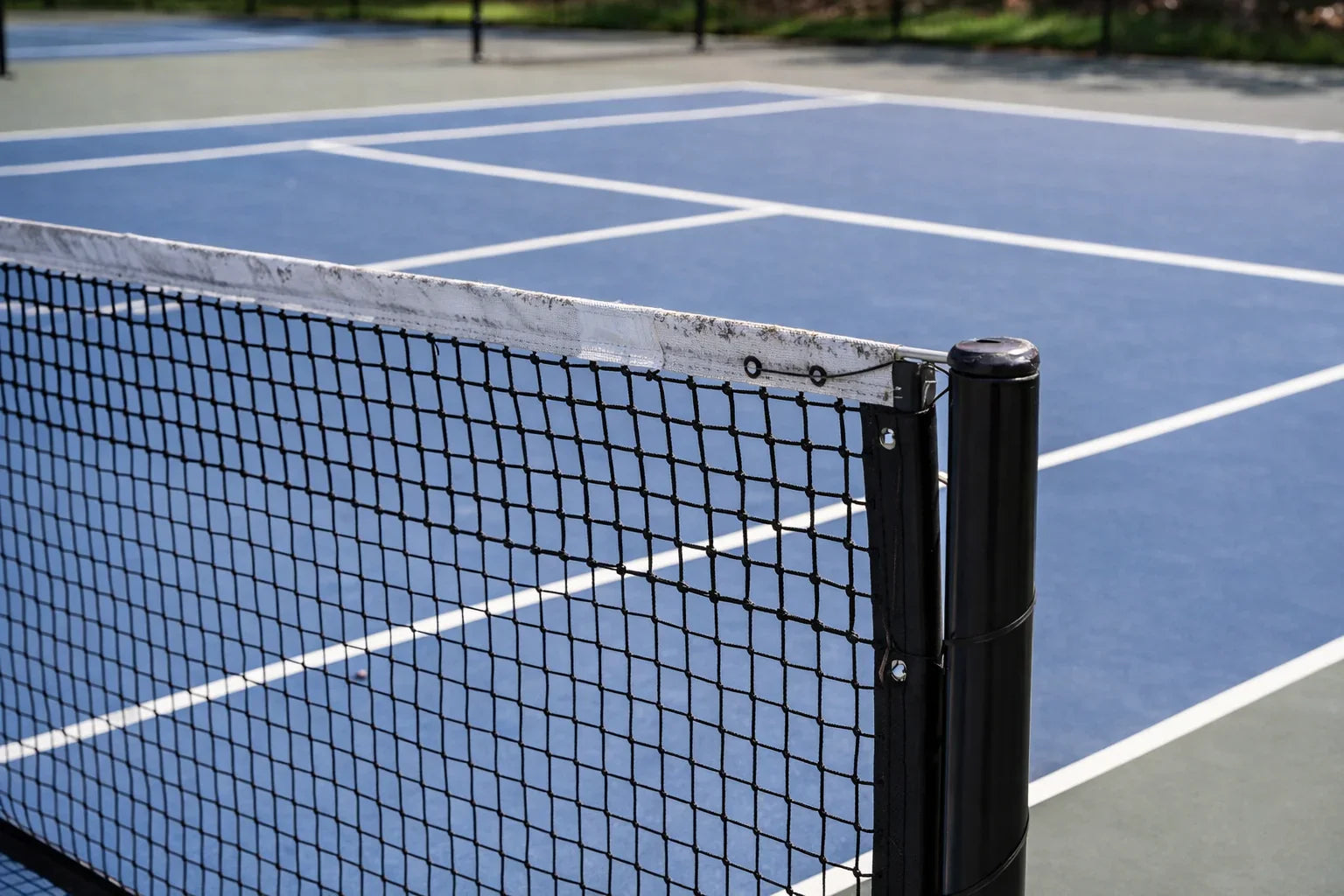 Gros plan sur un filet de pickleball noir installé sur un terrain bleu en extérieur.