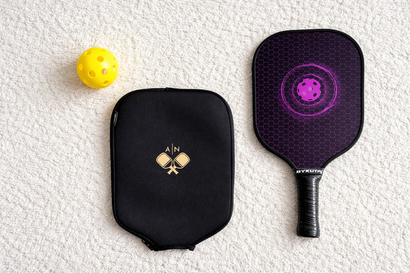 Housse de protection noire et raquette de pickleball avec balle jaune.