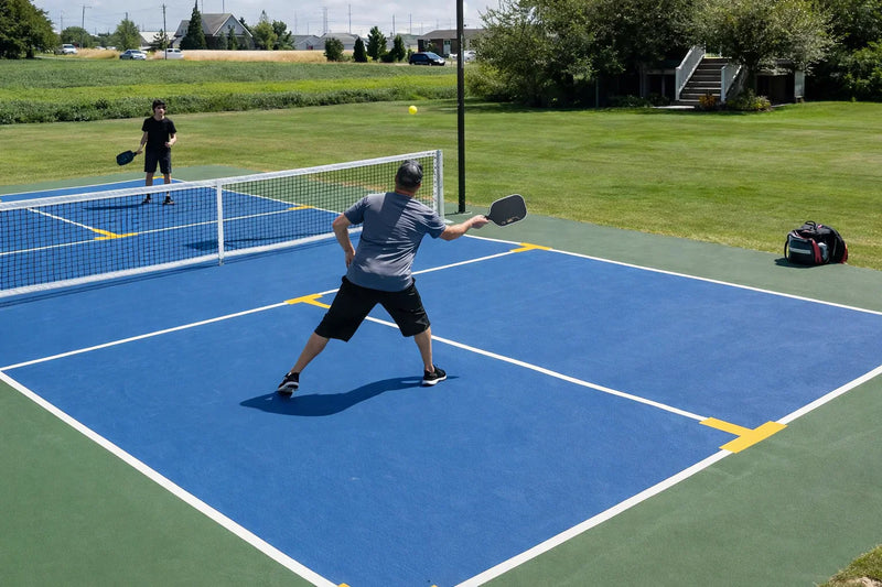 Joueurs de pickleball en pleine partie sur un terrain bleu avec marquages officiels en extérieur.