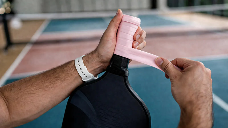 Pose d'un surgrip sur le manche d'une raquette de pickleball par un joueur.
