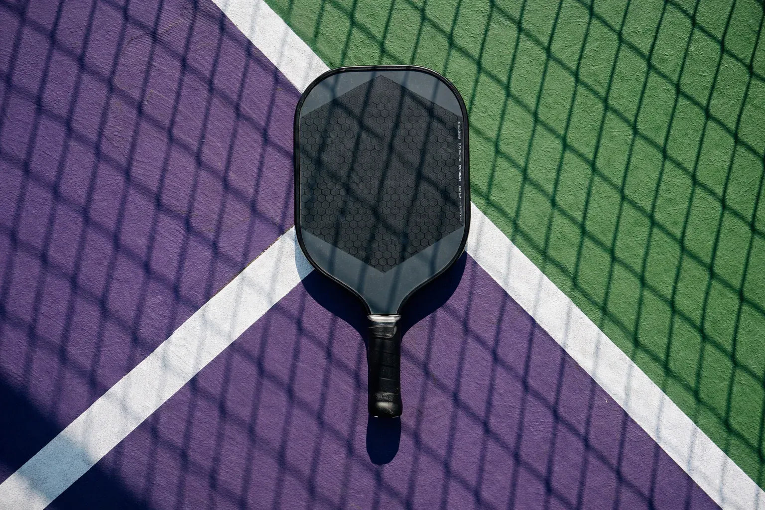  Raquette de pickleball posée sur un terrain de sport bleu et vert.