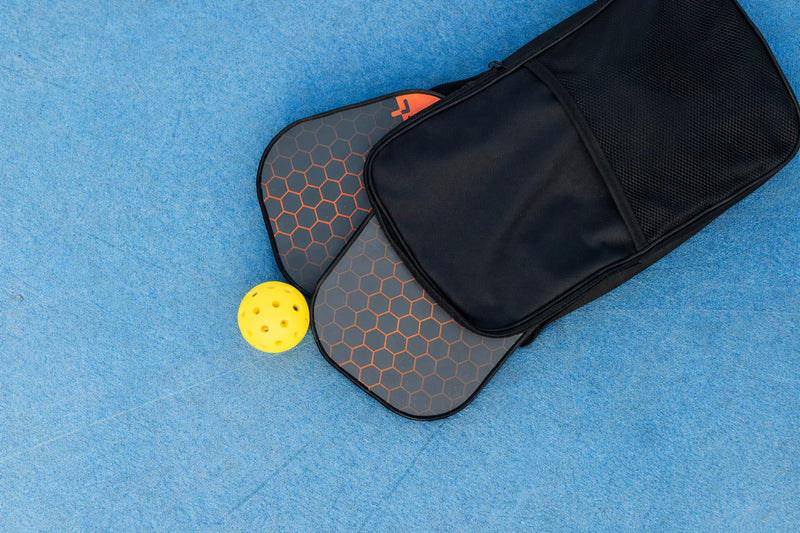 Sac de transport noir pour raquette de pickleball avec une balle jaune sur fond bleu.