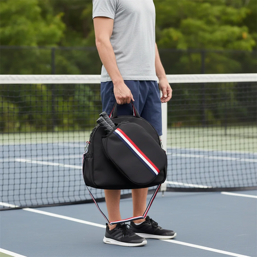 Joueur sur un court de pickleball portant à la main le sac de sport noir à sangles tricolores, montrant la housse extérieure contenant deux raquettes.